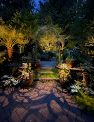 A winding garden path lined with lanterns and trimmed hedges in the evening