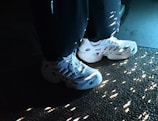 White sneakers with a futuristic design are highlighted by soft lighting, casting scattered reflections on a textured surface.