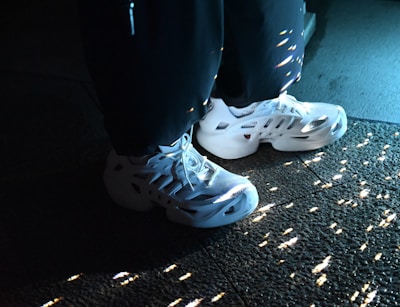 White sneakers with a futuristic design are highlighted by soft lighting, casting scattered reflections on a textured surface.
