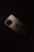 A smartphone with a sleek, metallic finish is placed on a dark surface. The device features a prominent camera module with multiple lenses and an Apple logo in the center.