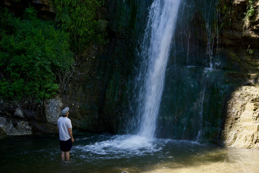 a man standing in the water near a waterfall