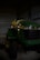 A green and yellow riding lawn mower is parked inside a dimly lit metal shed. The floor is made of concrete, and the shed walls are made of corrugated metal. The brand logo is visible on the front of the mower.