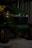 A green John Deere X320 lawn tractor is parked inside a dimly lit garage or shed. The tractor has yellow accents and features large black tires. The setting appears industrial with metal walls in the background.