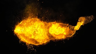 A vivid explosion of fiery orange and yellow hues creates a dynamic formation against a dark background. The bright, glowing area resembles molten lava or an intense burst of energy.