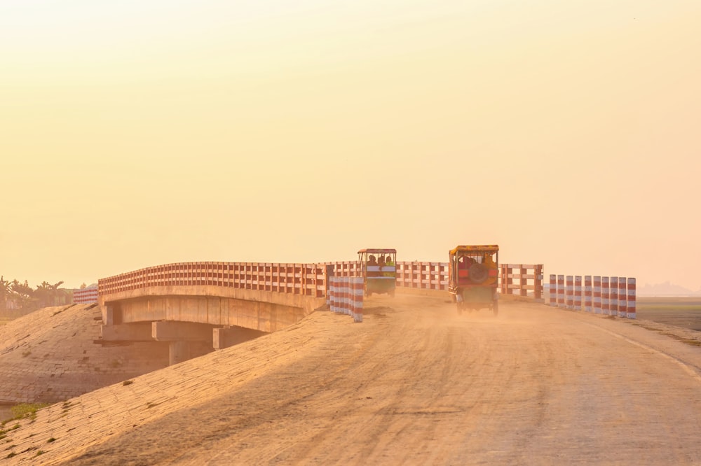 a truck driving down a dirt road next to a bridge