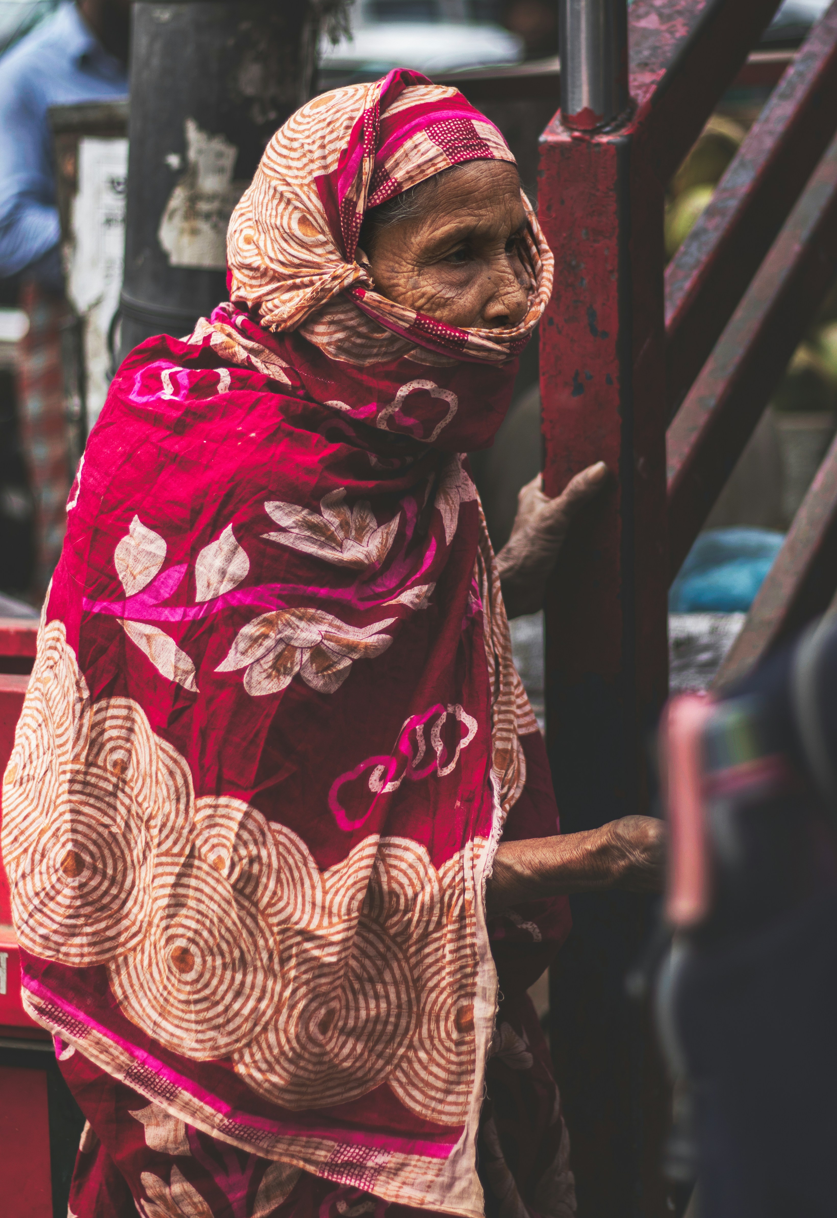 a woman in a red and gold shawl standing on a street