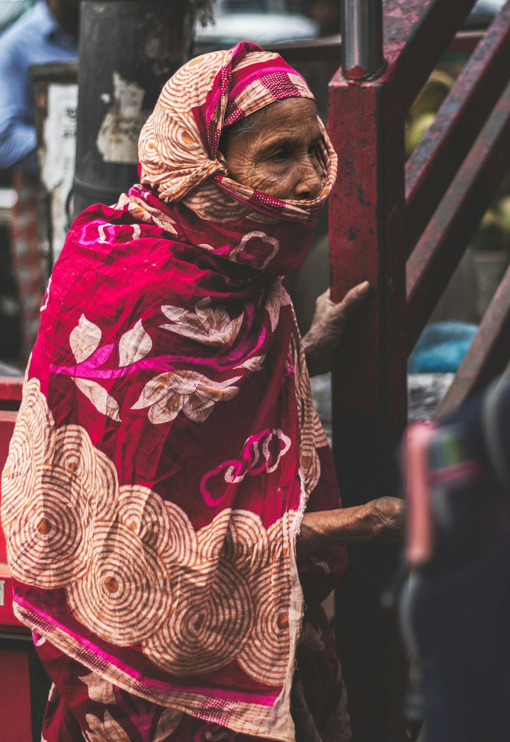 a woman in a red and gold shawl standing on a street