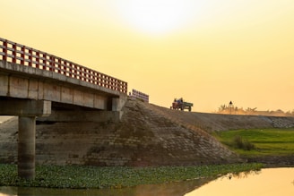 Heavy machinery compacting freshly laid dambar on a bridge deck at sunset.