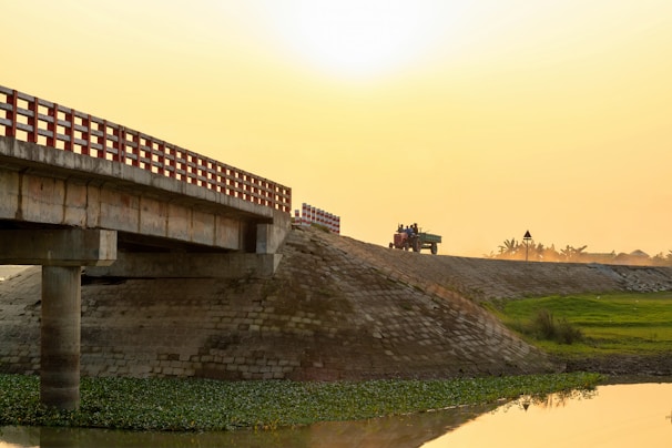 Heavy machinery compacting freshly laid dambar on a bridge deck at sunset.
