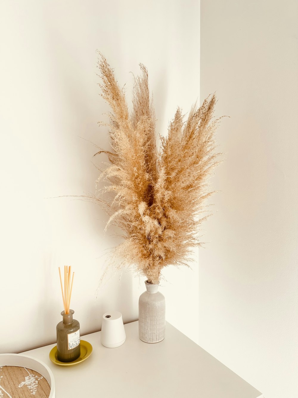 a white table topped with a vase filled with dry grass