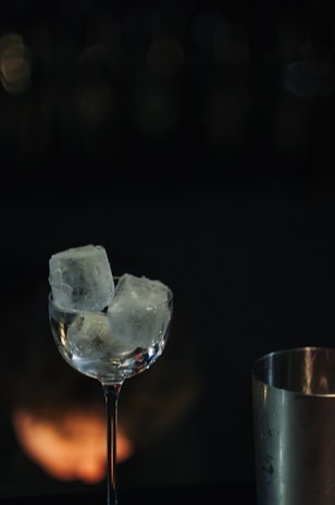 A bartender carefully placing a large block of clear ice into a cocktail shaker in a dimly lit bar.