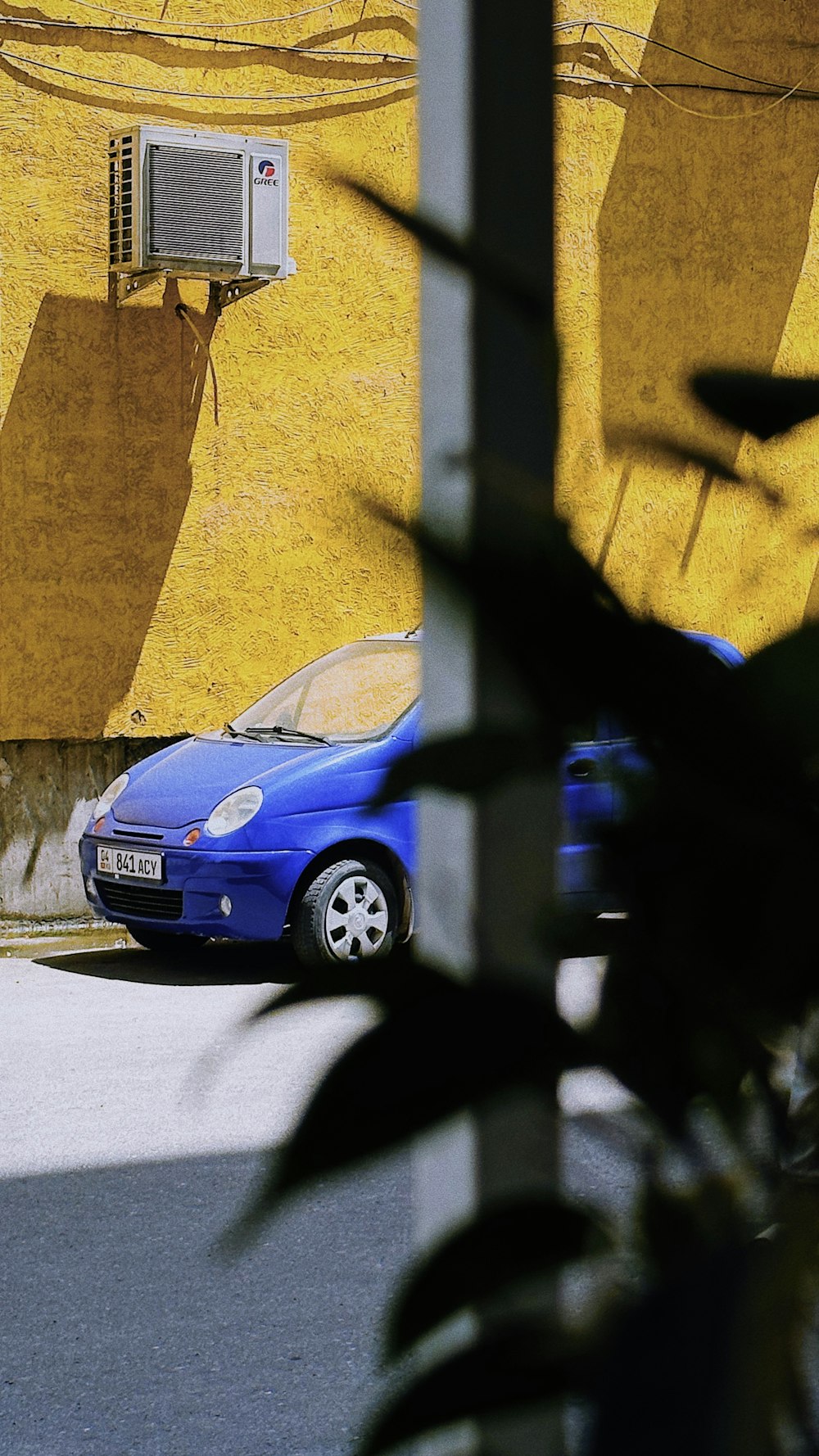 a blue car parked in front of a yellow wall