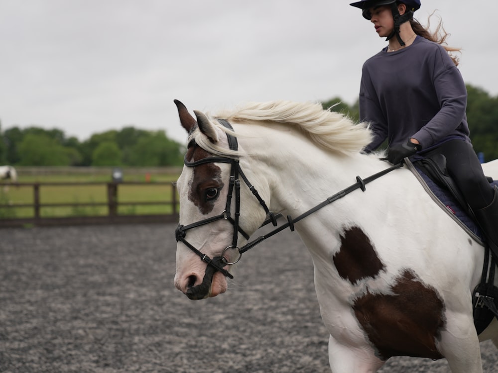 a woman riding on the back of a white and brown horse