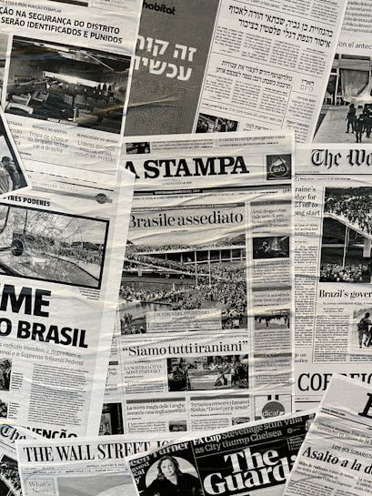The image contains a collage of various international newspaper front pages, featuring headlines and images related to global news events. The papers have sections in different languages such as English, Italian, and Hebrew. Prominent topics include political issues and events, with accompanying black-and-white photographs.