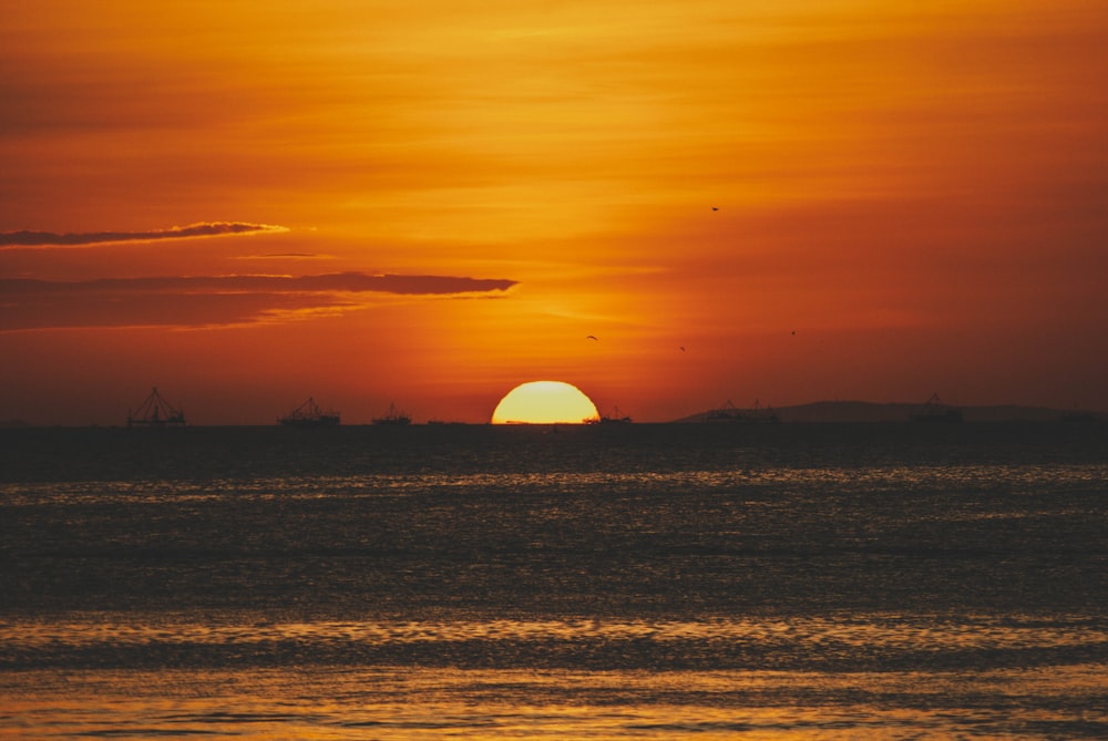 the sun is setting over the ocean with ships in the distance