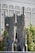 A large outdoor stone sculpture features two tall, abstract rock forms with smooth surfaces and cut-out holes. Figures of people are integrated into the sculpture, standing or seated. The backdrop includes a modern building with glass windows and columns, and greenery like trees.