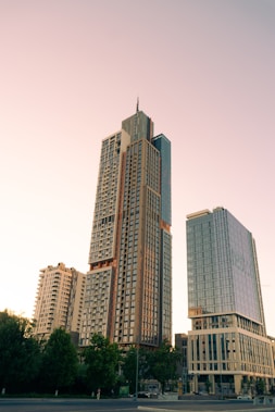 Several modern high-rise buildings captured in the early evening, with a clear sky and soft lighting. Tall residential or office structures feature a contemporary architectural style, surrounded by some green trees.