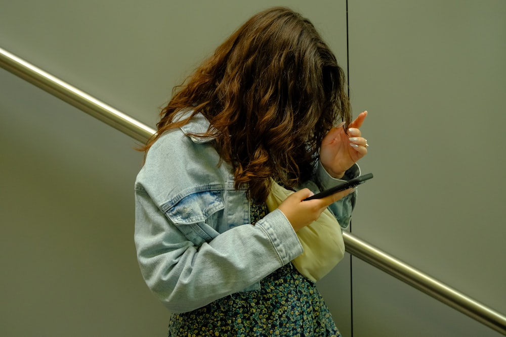 a young girl holding a cell phone while standing in front of a wall