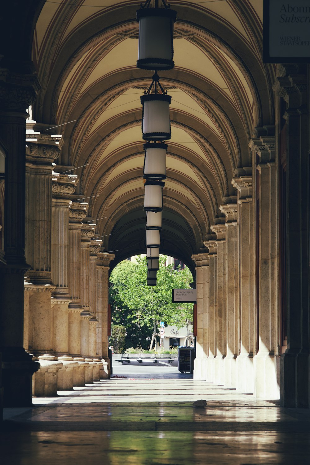 a long hallway with columns and lamps hanging from the ceiling