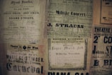 A collage of vintage posters featuring various advertisements and event announcements in German and French. The posters have a yellowed, aged appearance and display text in various fonts, some bold and decorative. Prominent names like Strauss and Geislinger are visible, indicating music concerts and theater productions.