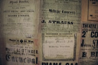 A collage of vintage posters featuring various advertisements and event announcements in German and French. The posters have a yellowed, aged appearance and display text in various fonts, some bold and decorative. Prominent names like Strauss and Geislinger are visible, indicating music concerts and theater productions.