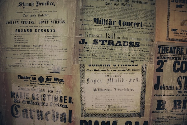 A collage of vintage posters featuring various advertisements and event announcements in German and French. The posters have a yellowed, aged appearance and display text in various fonts, some bold and decorative. Prominent names like Strauss and Geislinger are visible, indicating music concerts and theater productions.