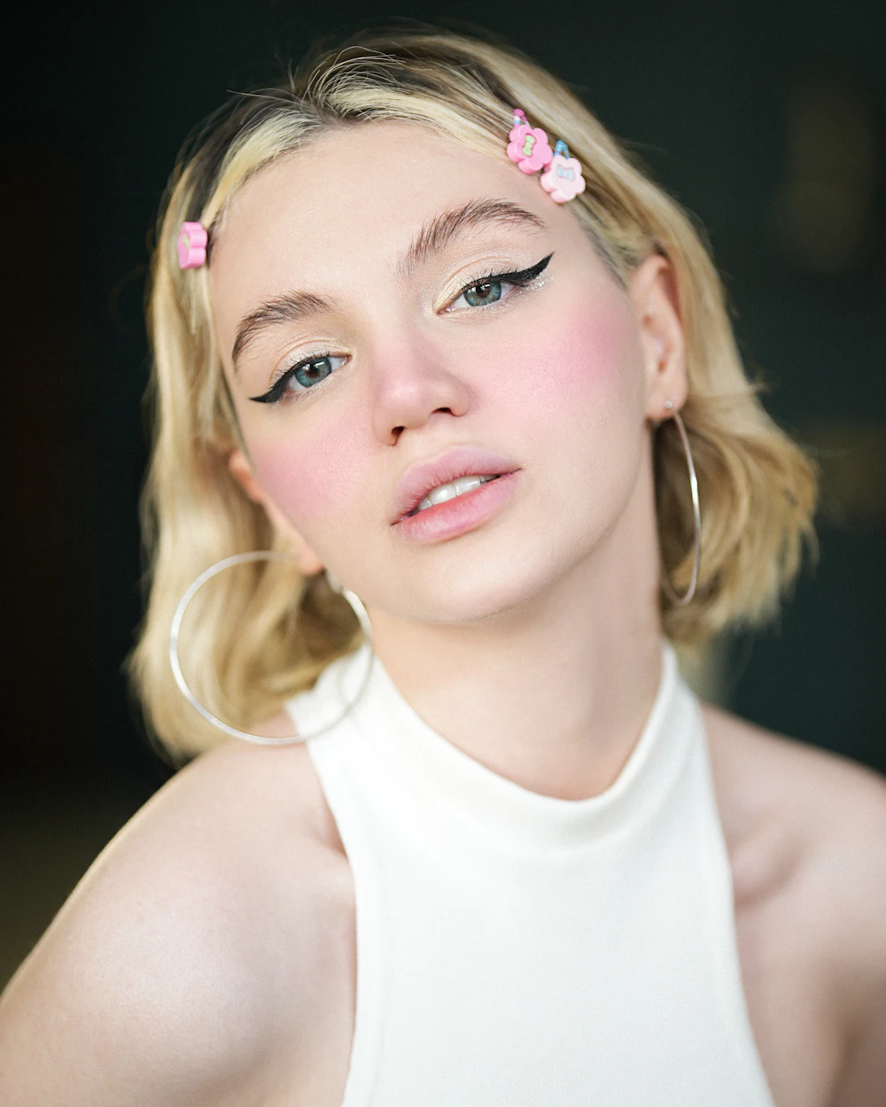Margaux in a white halter top with flower clips in her hair, looking into the camera.