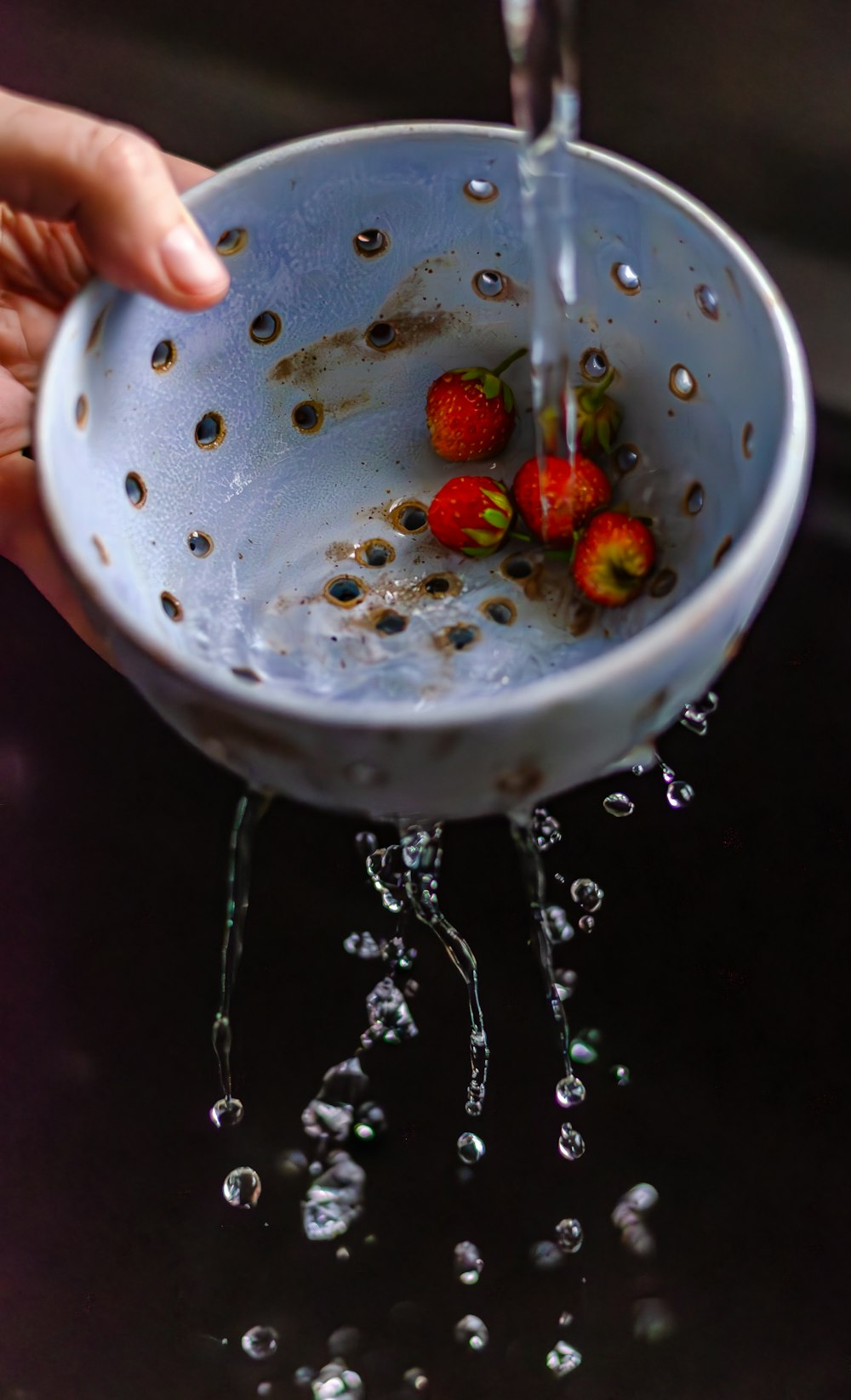 a person is holding a colander with strawberries in it