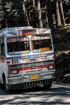 A sleek white Jay Ambe tour bus parked by a scenic Indian highway at sunset.