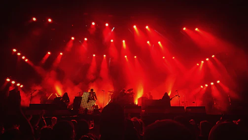 A shadowy, intense close-up of the band members performing live under deep red stage lights.