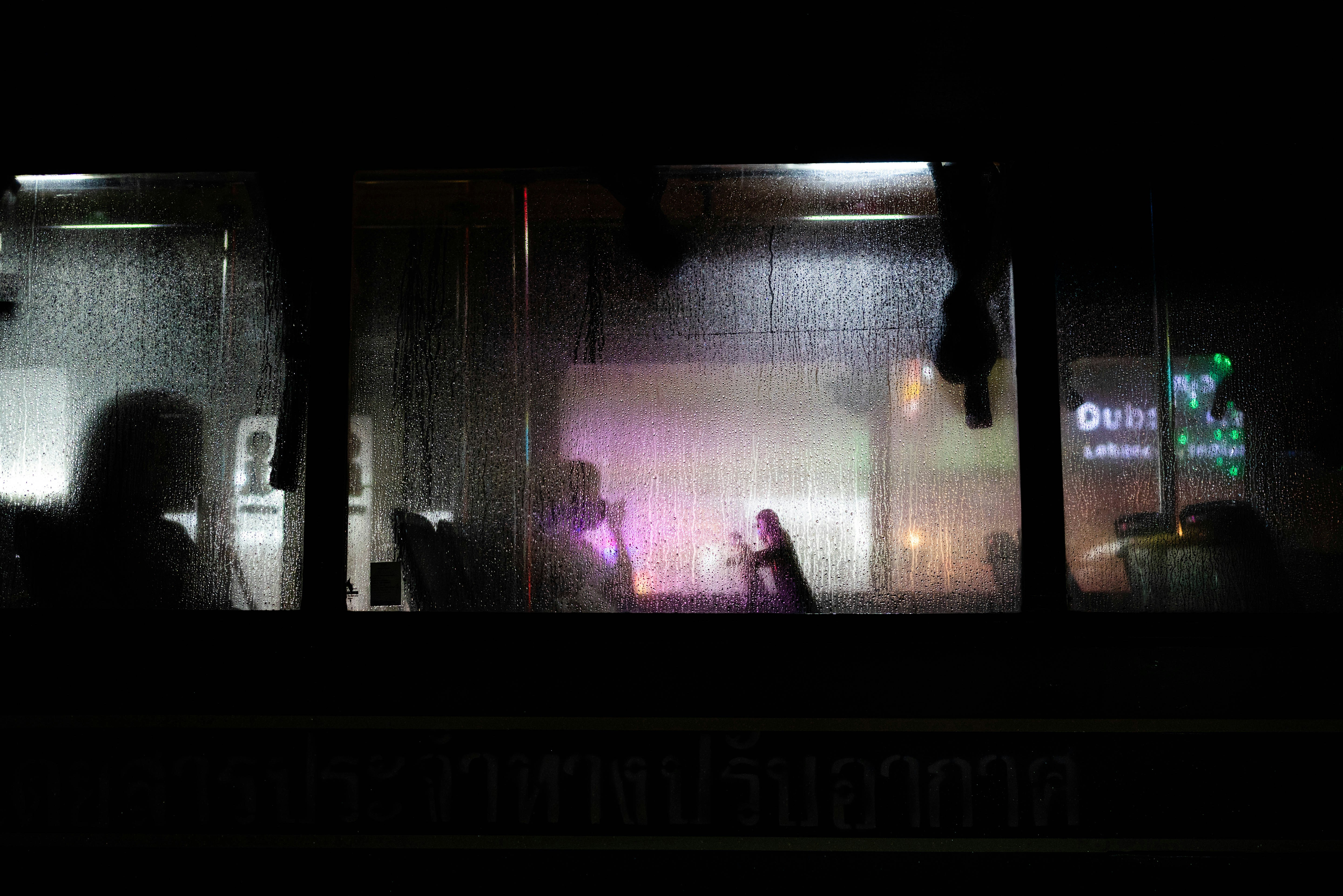 Rainy bus window at night with silhouetted figures