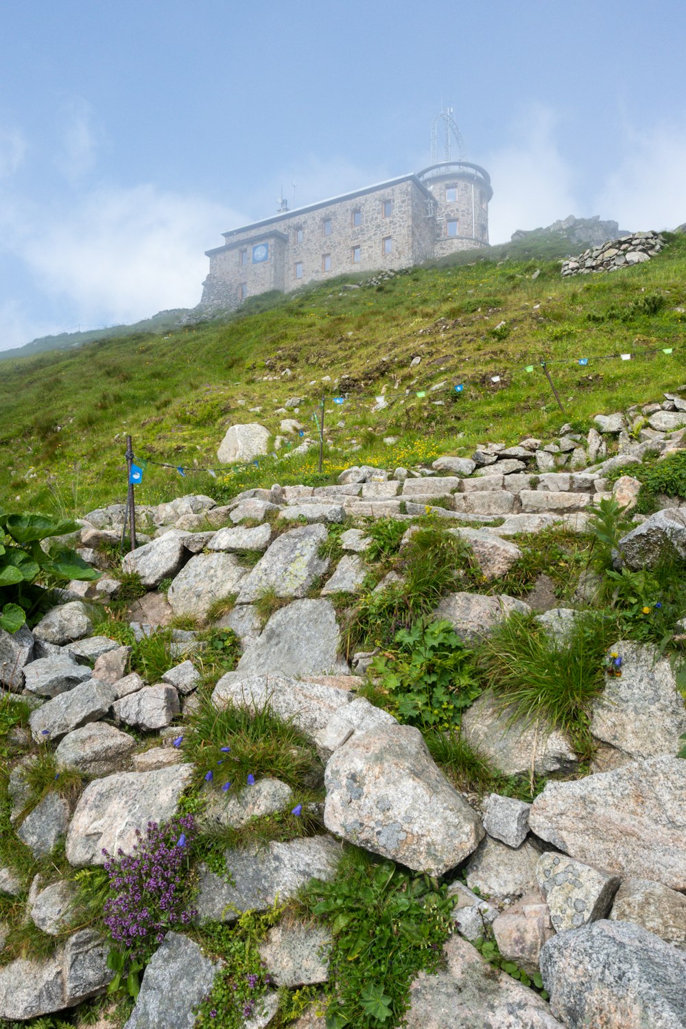 Ein Gebäude auf einem Hügel, der mit Gras und Felsen bedeckt ist