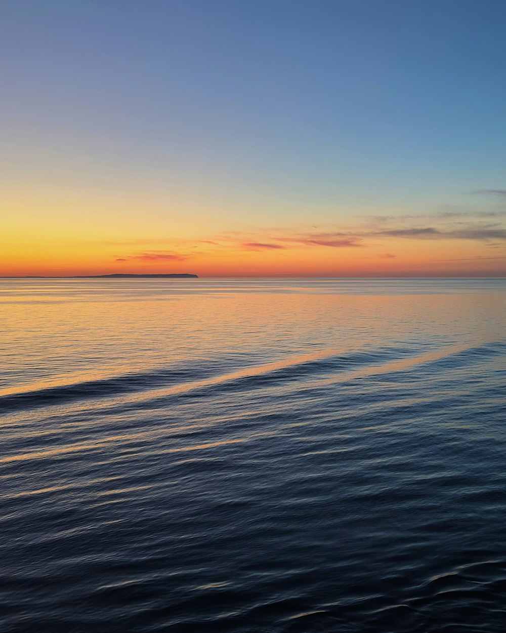 the sun is setting over the ocean with a wave in the foreground