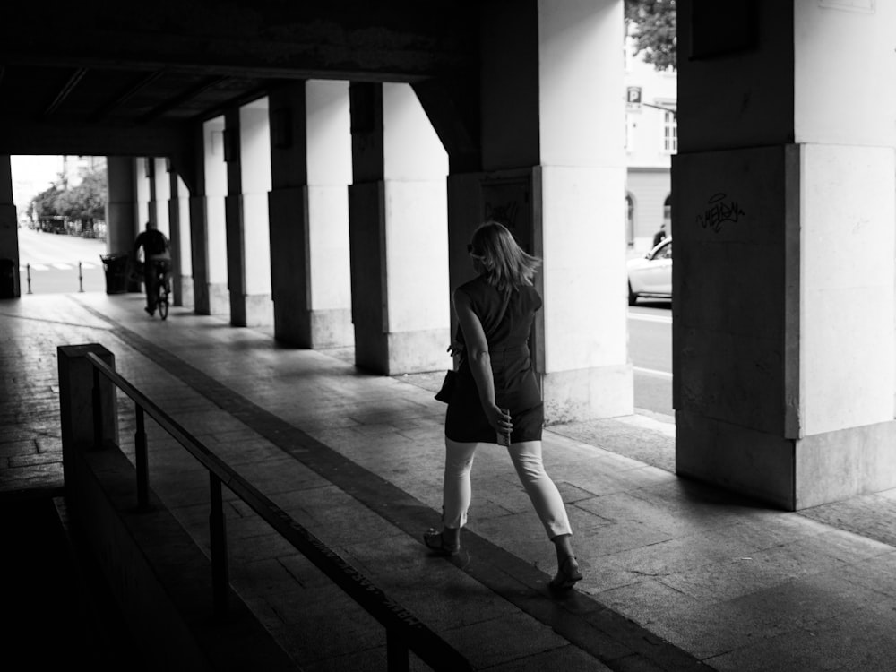 a black and white photo of a woman walking down a sidewalk