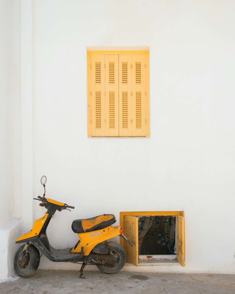 a yellow scooter parked next to a white wall