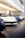 Displayed in a showroom, several luxury sports cars are lined up in a row on a polished wooden floor. The cars are primarily in colors like white, blue, black, and yellow, and are parked under modern, bright lighting, reflecting a clean and pristine environment.