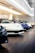 Displayed in a showroom, several luxury sports cars are lined up in a row on a polished wooden floor. The cars are primarily in colors like white, blue, black, and yellow, and are parked under modern, bright lighting, reflecting a clean and pristine environment.
