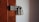 A robust silver padlock is securely fastened to a heavily weathered metal latch on a wooden door. The wooden surface shows signs of age with its faded brown color and visible screw holes.