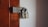 A robust silver padlock is securely fastened to a heavily weathered metal latch on a wooden door. The wooden surface shows signs of age with its faded brown color and visible screw holes.