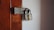A robust silver padlock is securely fastened to a heavily weathered metal latch on a wooden door. The wooden surface shows signs of age with its faded brown color and visible screw holes.
