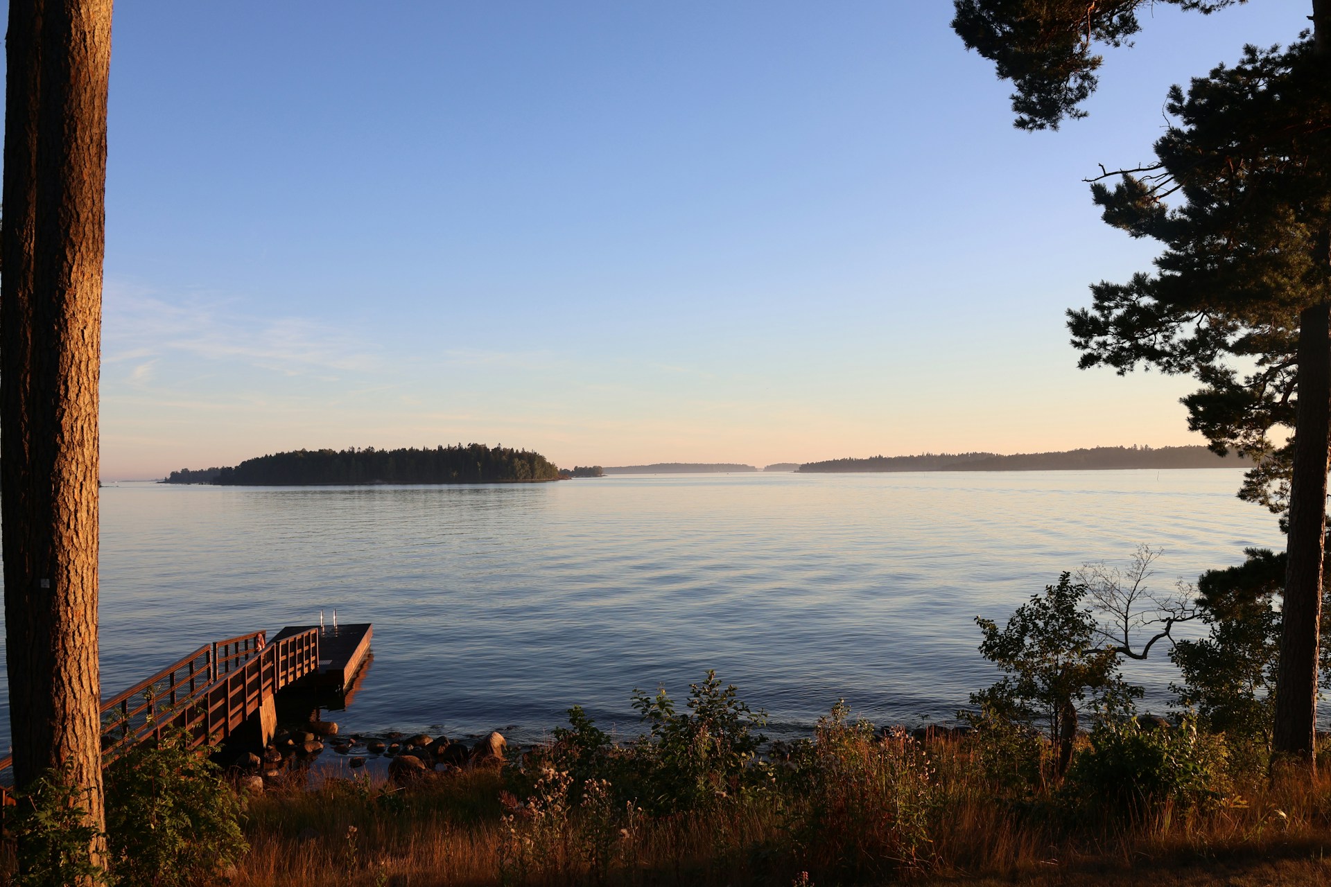 A serene view of a sunset over a tranquil lake, with a wooden dock leading to the water.