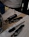 A table holds a variety of items including a fritz-kola branded bottle opener, a pen, and metallic multi-tools. The surface is covered with white fabric and a cardboard piece, while other items like a blue box and documents are partially visible.