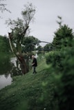 An excited beginner angler holding a fishing rod with a freshly caught fish beside a peaceful river.