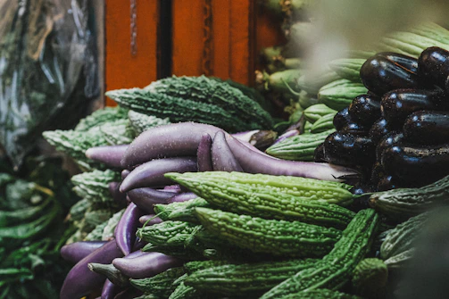 Exotic vegetables like okra and bitter melon arranged elegantly on a wooden table.