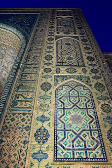 Intricate geometric patterns and ornate calligraphy on a tall wall, featuring blue and turquoise tiles creating an elaborate design. The artwork includes a series of repeating motifs and arches that highlight the precision of traditional craftsmanship.