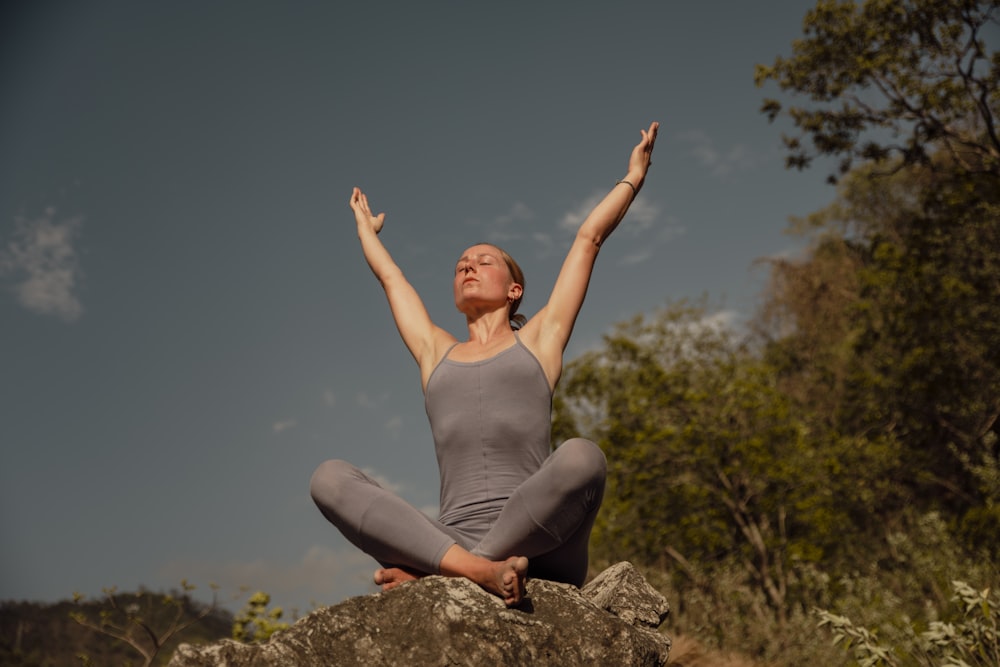 a woman is sitting on a rock doing yoga