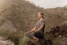 a woman sitting on top of a rock in a yoga position