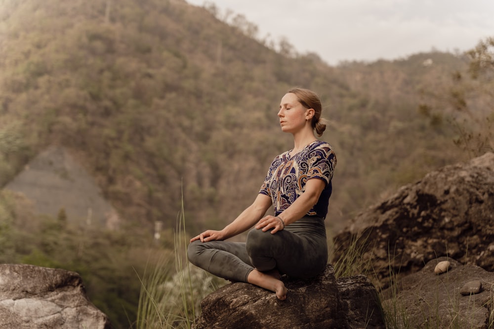 uma mulher sentada em cima de uma rocha em uma posição de ioga