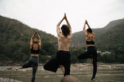 Participants sitting cross-legged on river rocks practicing yoga at sunrise, with mist rising from the water.