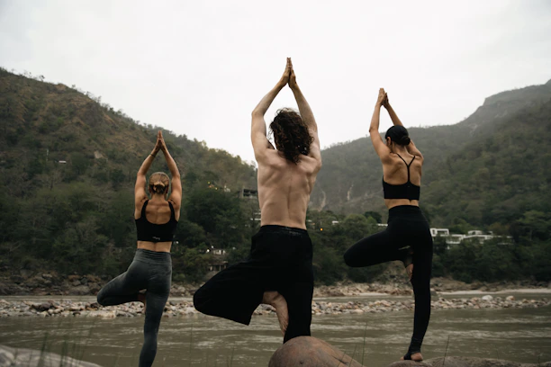 People practicing yoga outdoors surrounded by lush greenery and mountains.